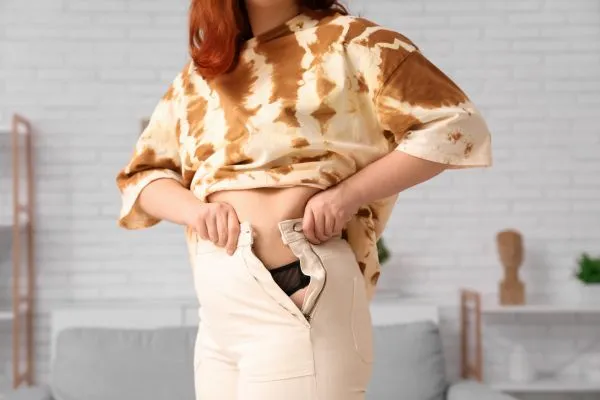 Image of woman trying to do her trousers up after pregnancy weight gain Birchfield